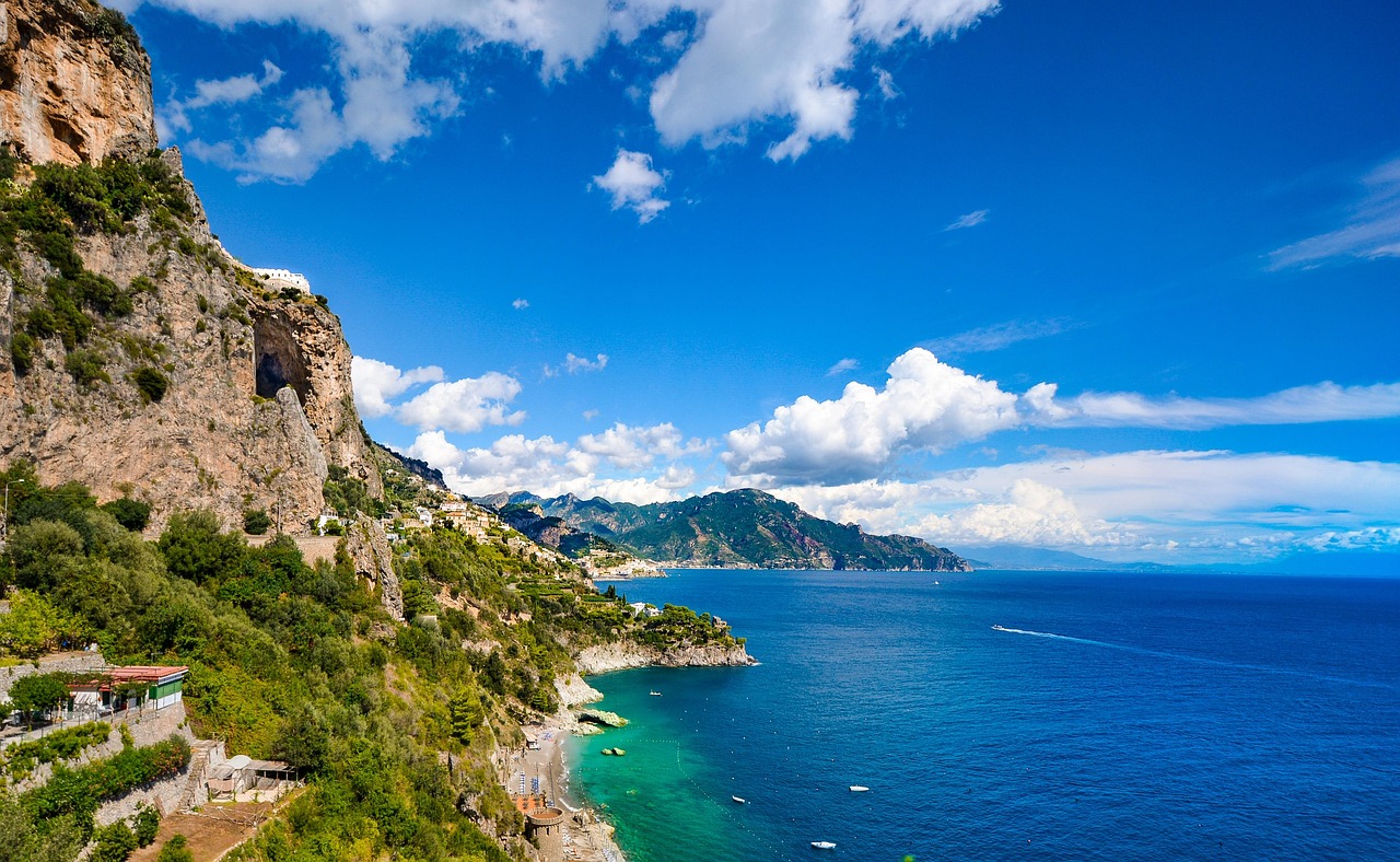 Scenic view of the Italian coastline with turquoise water and cliffs under a bright blue sky, symbolizing Fight & Travel adventure holidays